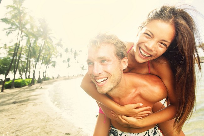 Happy young joyful couple having beach fun piggybacking laughing