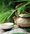 Teapot and cups on stone with bamboo leaves.