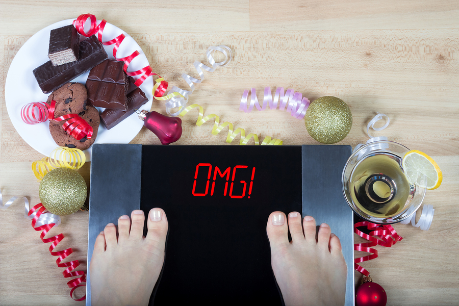 Digital scales with woman feet on them and sign"OMG!" surrounded by christmas decorations sweets and alcohol. Demonstrates consequences of surfeit and eating unhealthy food during Christmas holidays.